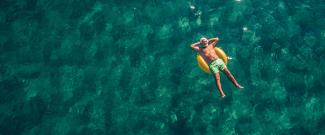 An older man relaxing and laying down in an inner tube on relaxing water.